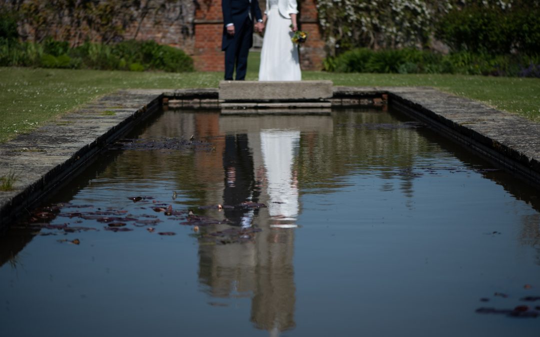 bride and groom reflected in pond at Goodnestone Park