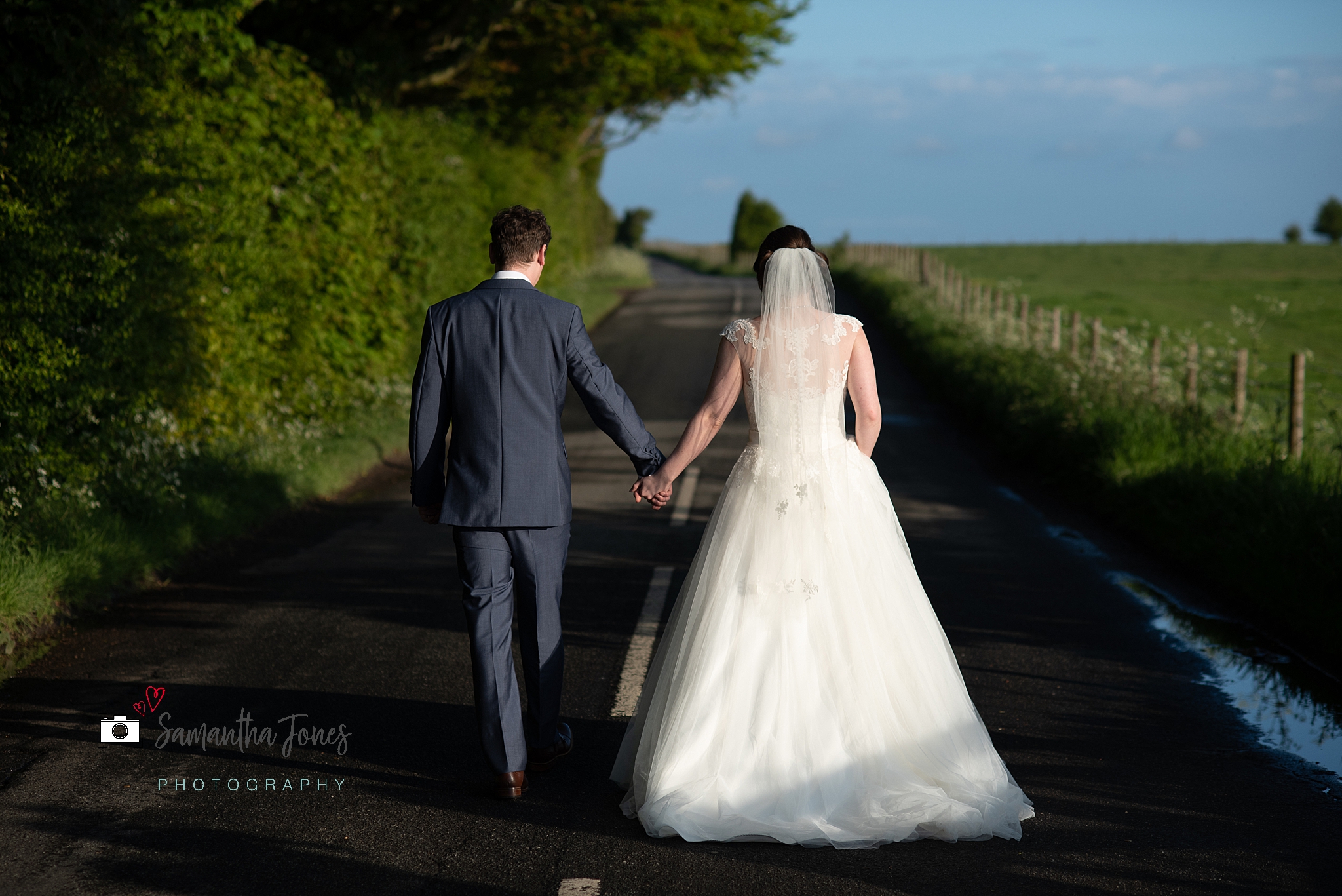 bride and groom walking along road in sunshine